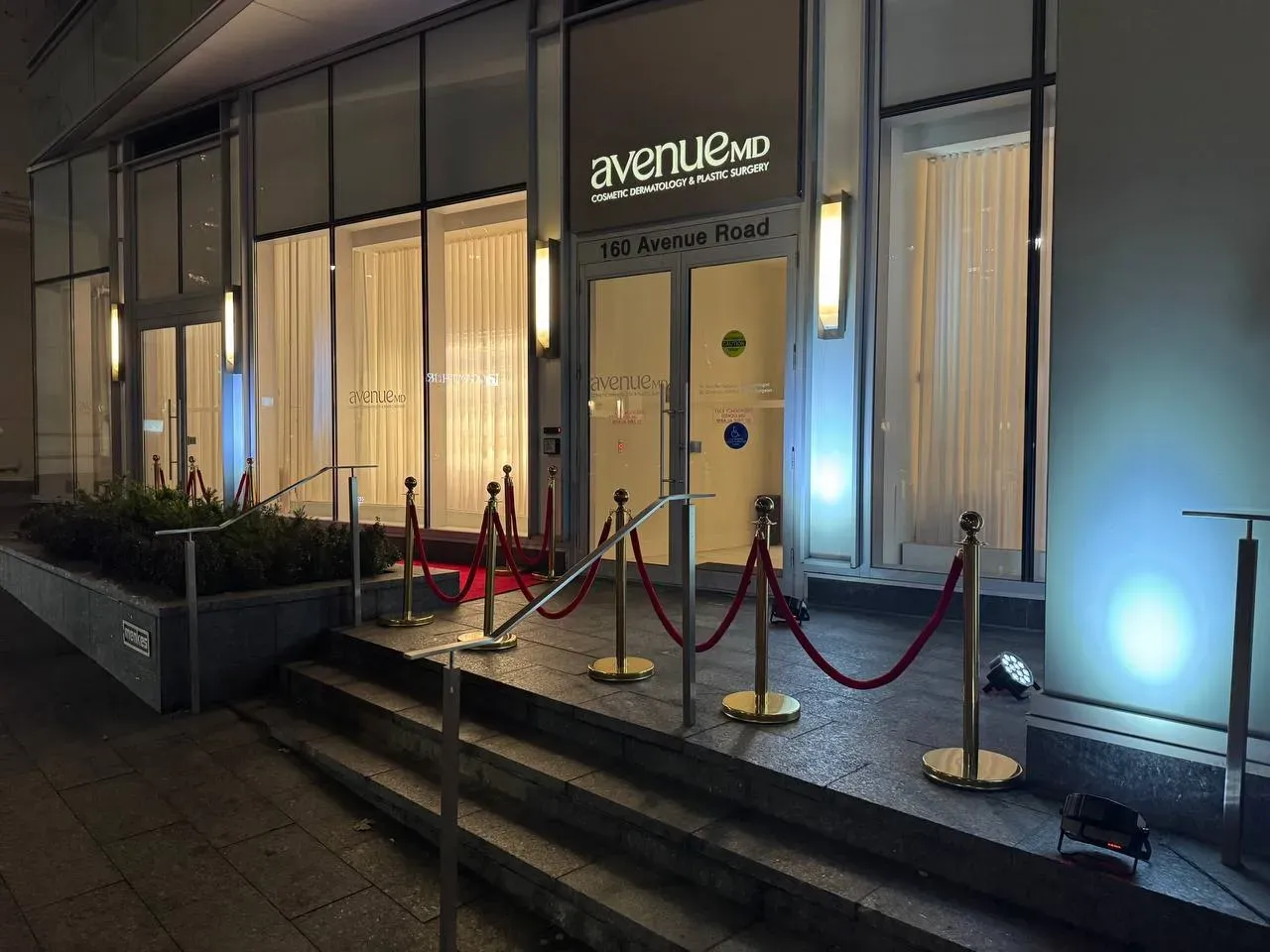 Gold rope stanchions with red velvet ropes lining a red carpet up the front steps at night